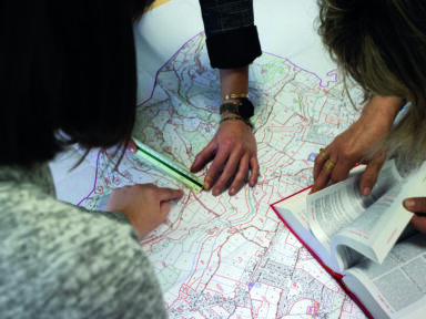 Trois agents du service urbanisme penchés sur une carte avec le code de l'urbanisme pour effectuer leur travail.